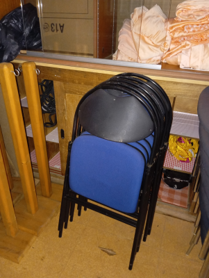Chaises empilées dans un local de rangement avec étagères et divers objets.