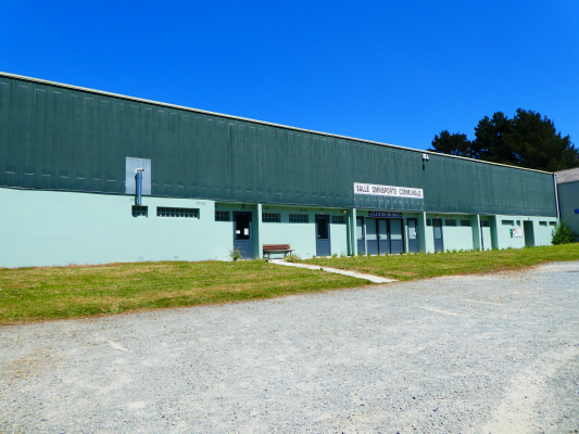 Bâtiment industriel avec entrée, enseigne et banc.