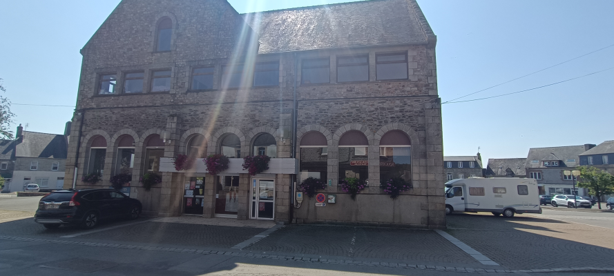 Bâtiment en pierre avec voitures et camping-car garés devant.
