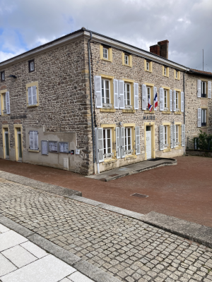 Bâtiment en pierre avec fenêtres, portes, drapeaux, et boîtes aux lettres. Rue pavée.