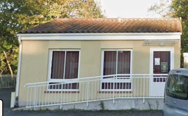 Maison avec toit en tuiles, murs beiges, trois fenêtres avec rideaux bruns, porte d'entrée, rampe blanche et voiture garée.