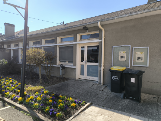 Bâtiment avec porte, fenêtres, deux poubelles et fleurs devant.