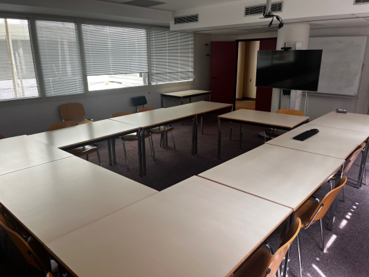 Salle avec tables, chaises, écran, vidéo projecteur et tableau.