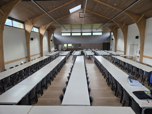 "Salle avec rangées de tables, chaises, et tableau à l'avant."