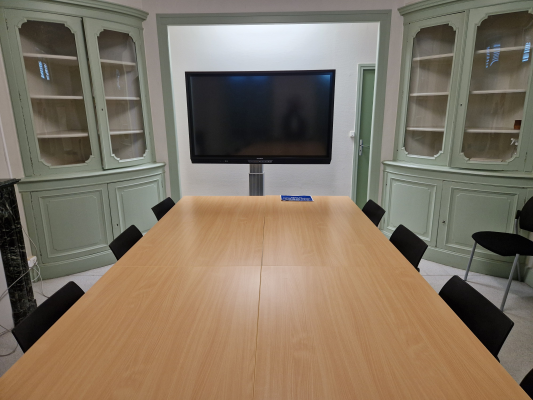 Salle de réunion avec table, chaises, écran et armoires.