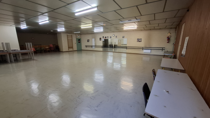 Salle spacieuse avec tables, chaises, barres de danse, horloge, tableaux et éclairage au plafond.