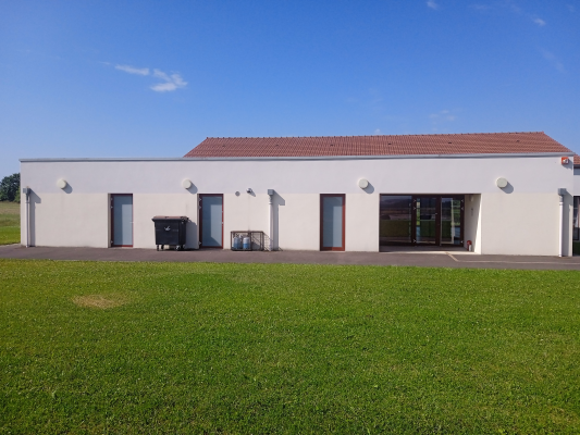 Bâtiment blanc avec toiture rouge, portes et fenêtres, poubelle et table à l'extérieur.