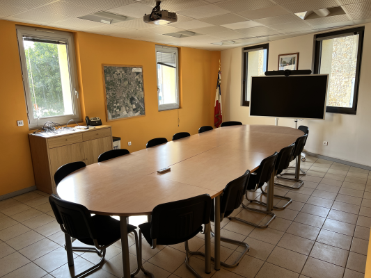 Salle de réunion avec table ovale, chaises, écran, vidéo projecteur et étagère.