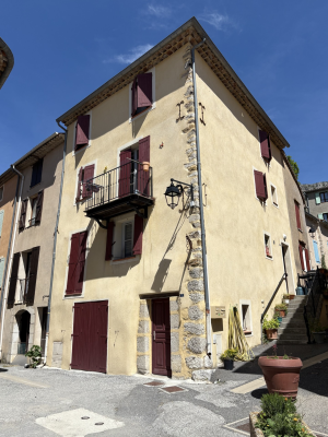 Maison avec volets marrons, balcon, lanterne et pot de fleurs.