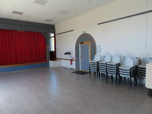 Salle avec rideau rouge, porte, chaises empilées et extincteur.