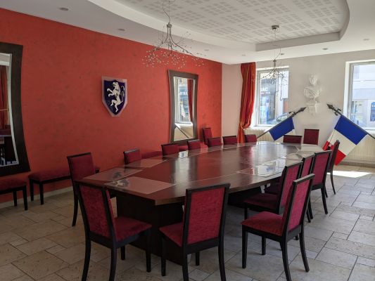Salle avec table, chaises, lustres, drapeaux et armoire.