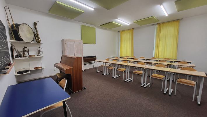 Salle de classe avec piano, instruments, bureaux, chaises, tableau et rideaux.