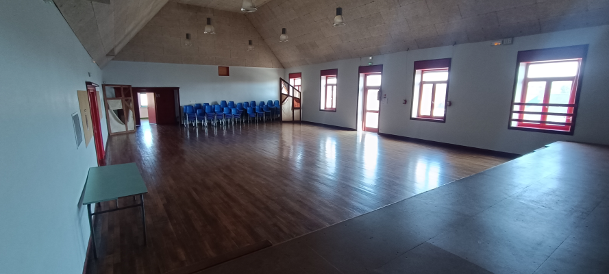 Salle vide avec parquet, chaises alignées, fenêtres, portes et table basse.