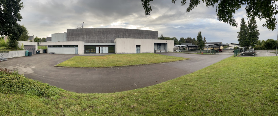 Bâtiment d'apparence industrielle avec des portes de garage, stationnement et verdure environnante.