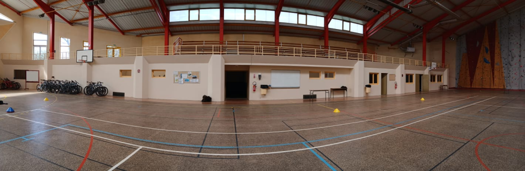 Gymnase avec vélos, table, tableau blanc, mur d'escalade et terrain de basket.