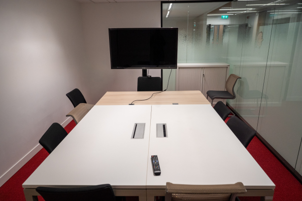 Salle de réunion avec table, chaises, écran, télécommande et armoire.