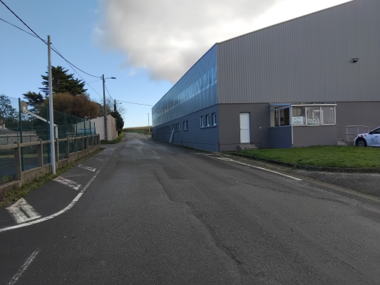 Route menant à un bâtiment industriel avec clôture, lampadaire et voiture.