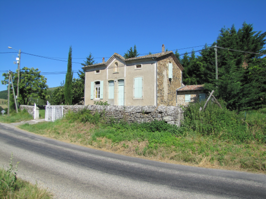 Maison de pierre avec fenêtres blanches, clôture et route.