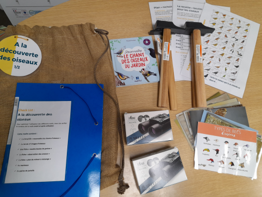 Sur une table, un kit d'observation d'oiseaux avec sac en toile, jumelles, marteaux, cartes d'identification d'oiseaux, brochures et liste de contrôle.