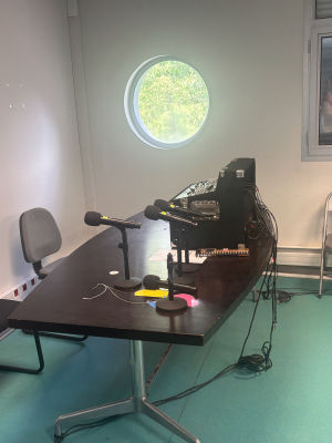 Studio d'enregistrement avec table de mixage, microphones, chaises et câbles.