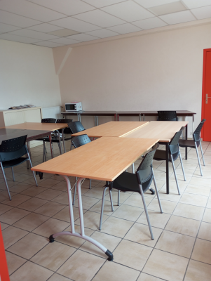 Salle avec tables, chaises, poste de travail surélevé et porte rouge.