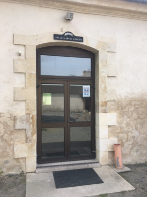 Entrée avec porte vitrée, paillasson, extincteur et enseigne.