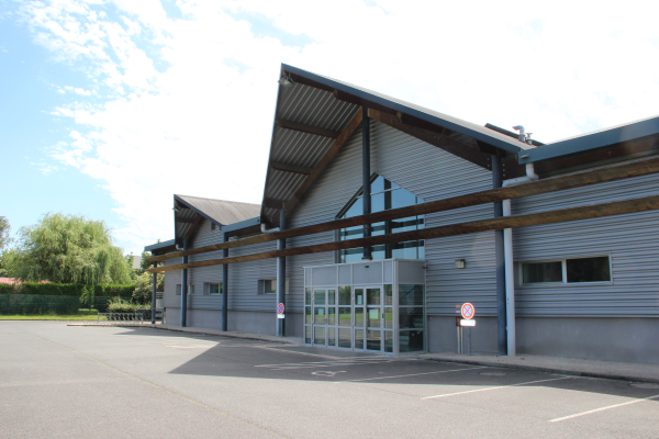 Bâtiment industriel avec entrée en verre, parking et arbre.