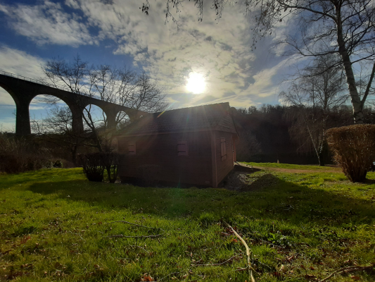 Cabane en bois près d'un pont ferroviaire sous un ciel partiellement nuageux.