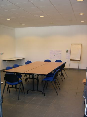 Salle avec tables, chaises, tableau blanc et paperboard.