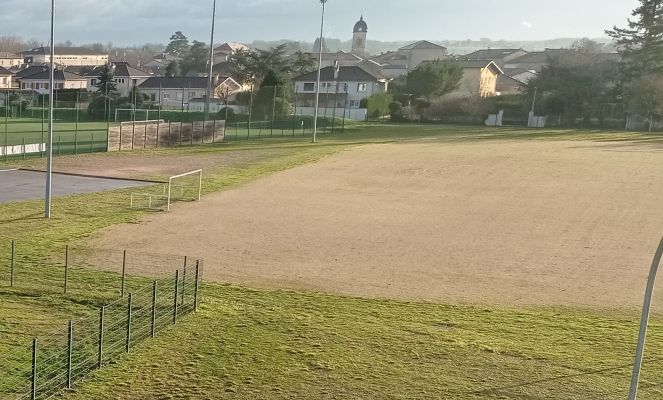 Terrain de sport avec but de football, piste d'athlétisme, clôtures et maisons en arrière-plan.