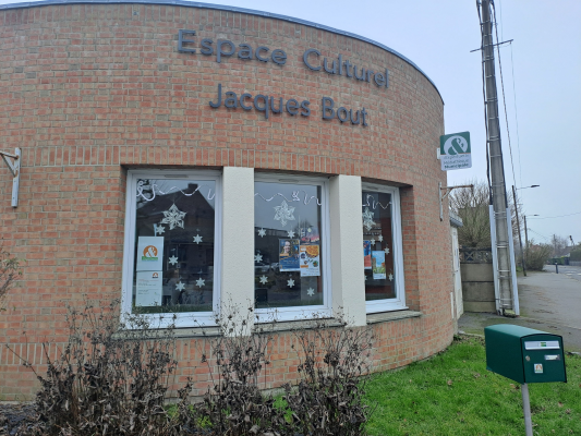 Bâtiment en brique avec enseigne "Espace Culturel Jacques Bout". Fenêtres décorées de flocons de neige et affiches. Boîte aux lettres verte à l'extérieur.
