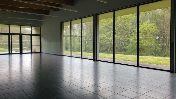 Salle vide avec grandes baies vitrées.