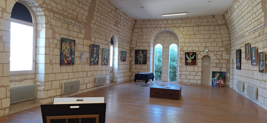 Salle avec murs en pierre, tableaux, fenêtres, tables, et radiateurs.