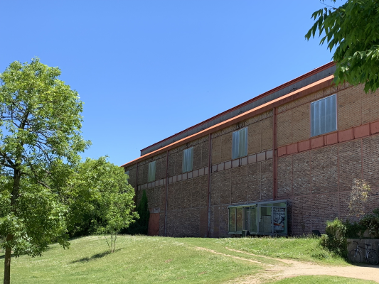 Bâtiment en brique avec fenêtres, pelouse, arbres et ciel bleu.