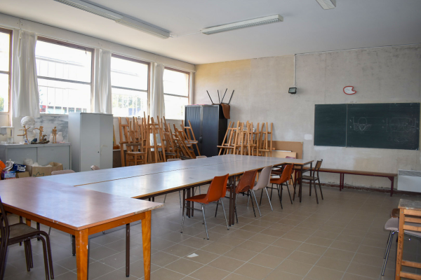 Salle de classe avec tableau noir, tables, chaises, fenêtres et armoire.