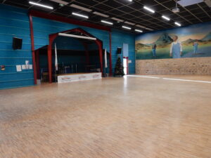 Salle spacieuse avec scène, mur décoré, porte, escalier et éclairage.