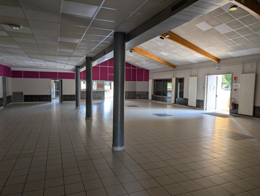 Grand espace vide avec colonnes, portes, fenêtres et sorties de secours. Sol carrelé, murs rose et plafond avec dalles.