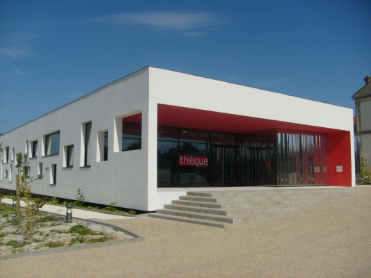 Bâtiment moderne avec façade blanche, grandes baies vitrées, entrée rouge, escalier et gravier.