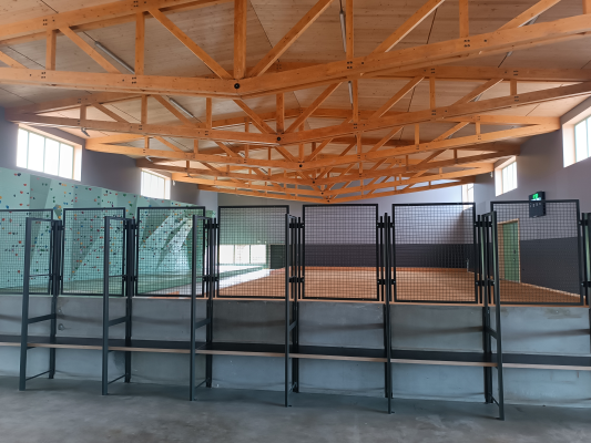 "Salle avec structure bois, tables, chaises, mur d'escalade vert et sol gris."