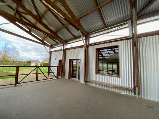 Atelier avec sol en béton, toit en tôle, poutrelles apparentes, porte et fenêtre.