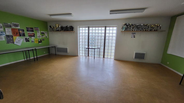 Salle spacieuse avec murs verts, tableaux d'affichage, étagères, portes vitrées, et radiateurs.