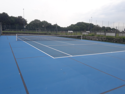 Terrain de tennis bleu avec filet, clôture et arbres en arrière-plan.