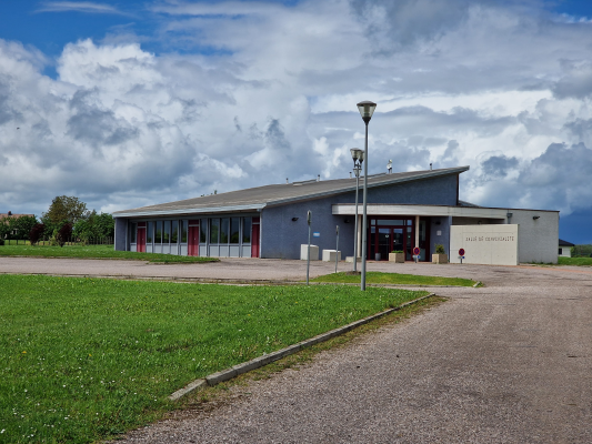 Bâtiment avec toiture plate, devantée par un lampadaire, une pelouse et une allée.