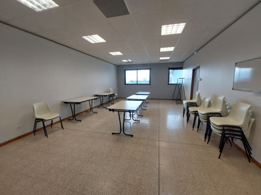 Salle avec tables, chaises, tableau blanc et fenêtre.