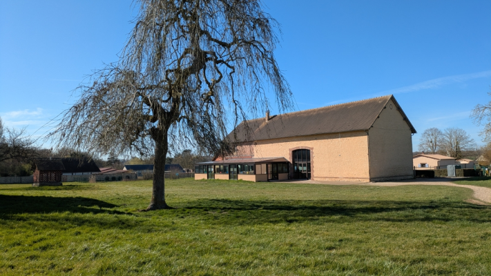 Bâtiment avec grand arbre devant, pelouse, ciel dégagé.