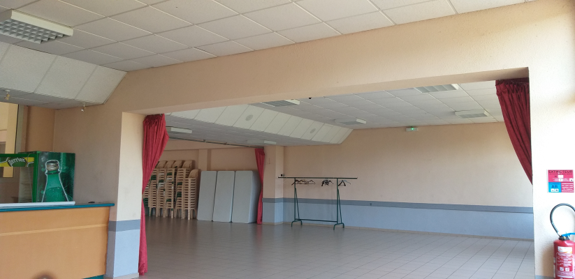 Salle vide avec rideaux, porteurs de vêtements, chaises empilées et extincteur.