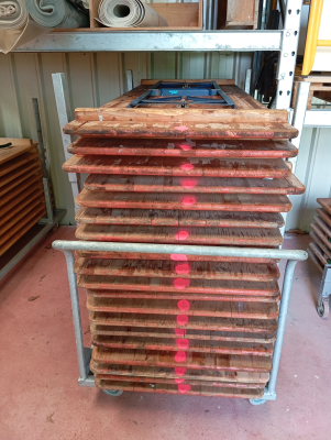 Empilement de planches en bois sur chariot métallique dans un entrepôt.