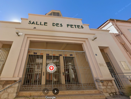 "Entrée de salle des fêtes avec grilles, portes vitrées, enseigne et lampes."