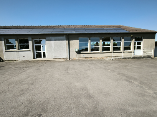 Bâtiment à un étage avec panneaux solaires sur le toit, entrées doubles vitrées, et porte d'entrée en verre. Parking en gravier devant.