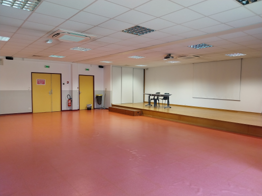 Salle avec tables, chaises, tableau, placard, portes et extincteur.